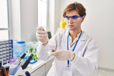 Young caucasian man scientist pouring liquid on plant sample at laboratory