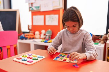 Adorable hispanic boy playing with maths puzzle game sitting on table at kindergarten