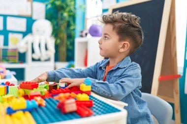 Adorable hispanic toddler playing with construction blocks sitting on table at kindergarten