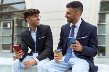 Two hispanic men business workers using smartphones drinking coffee at street