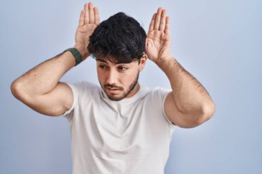 Hispanic man with beard standing over white background doing bunny ears gesture with hands palms looking cynical and skeptical. easter rabbit concept. 