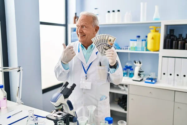 研究室で働いている灰色の髪を持つシニア科学者持っていますドル指して親指上へ側笑顔幸せなでオープン口 — ストック写真