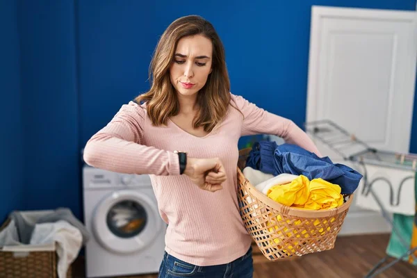 Young woman holding laundry basket checking the time on wrist watch, relaxed and confident