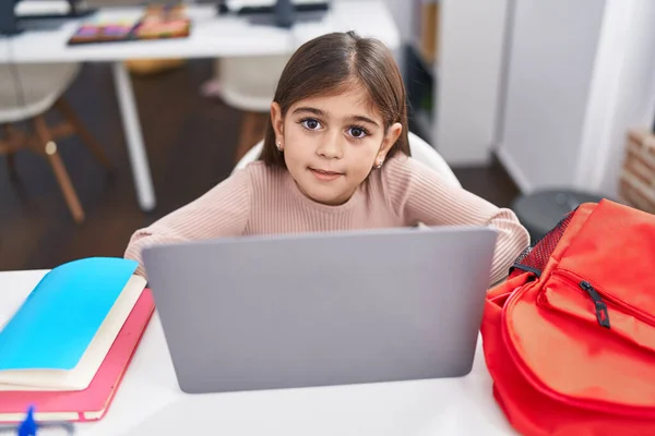 Adorable hispanic girl student using laptop sitting on table at classroom