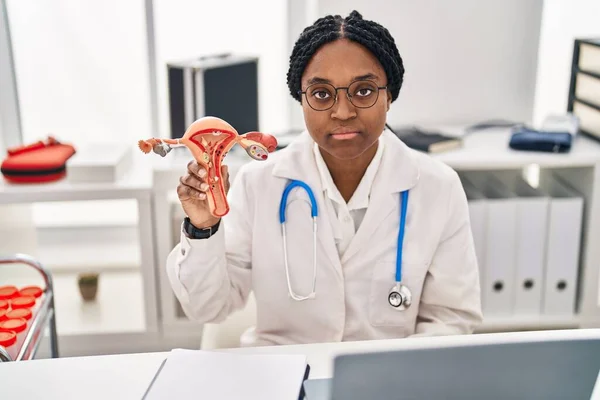 African american doctor woman holding anatomical model of female genital organ thinking attitude and sober expression looking self confident