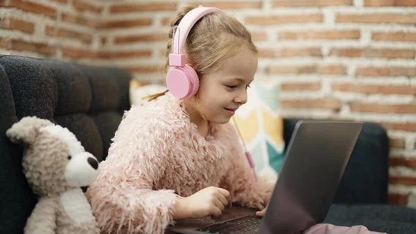 Adorable Blonde Girl Using Laptop Headphones Sitting Sofa Teddy Bear — Stok fotoğraf