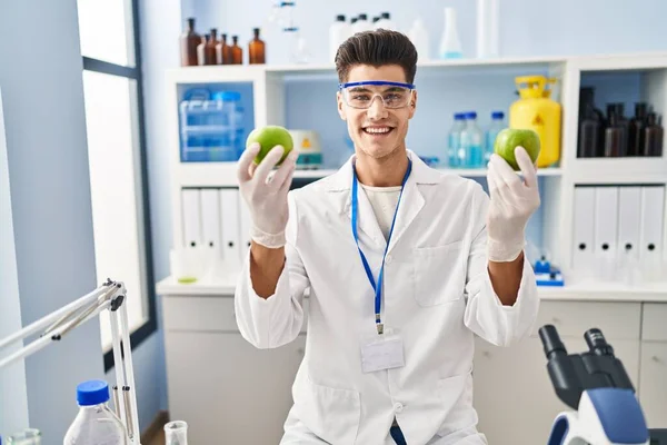 Young Hispanic Man Wearing Scientist Uniform Holding Apples Laboratory — ストック写真
