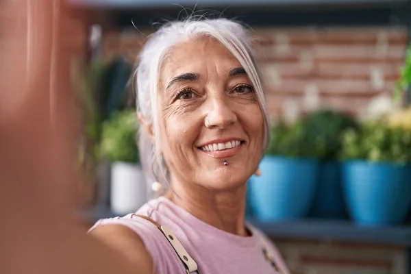 Middle age grey-haired woman florist smiling confident make selfie by camera at florist