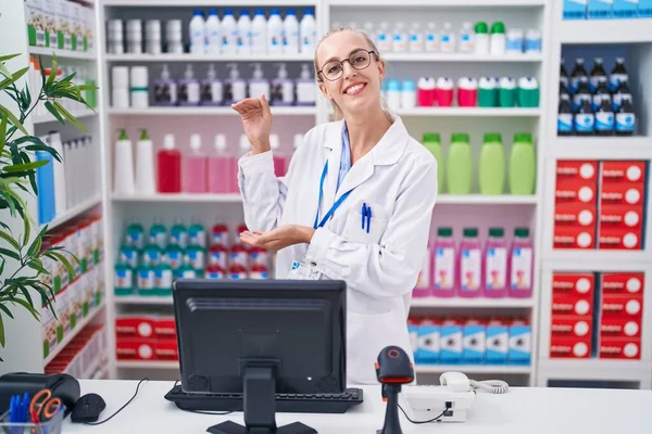 Young caucasian woman working at pharmacy drugstore gesturing with hands showing big and large size sign, measure symbol. smiling looking at the camera. measuring concept.
