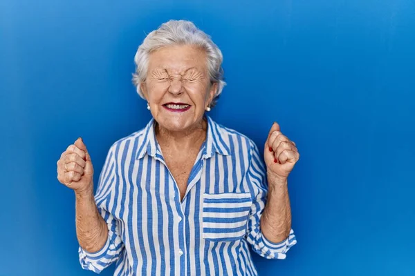 Starsza Kobieta Siwymi Włosami Stojąca Niebieskim Tle Podekscytowana Sukcesem Podniesionymi — Zdjęcie stockowe
