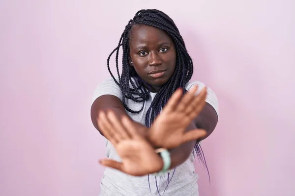 ピンクの背景の拒絶表現の上に立っている若いアフリカの女性負の記号を行う腕と手のひらを横断 怒っている顔 — ストック写真