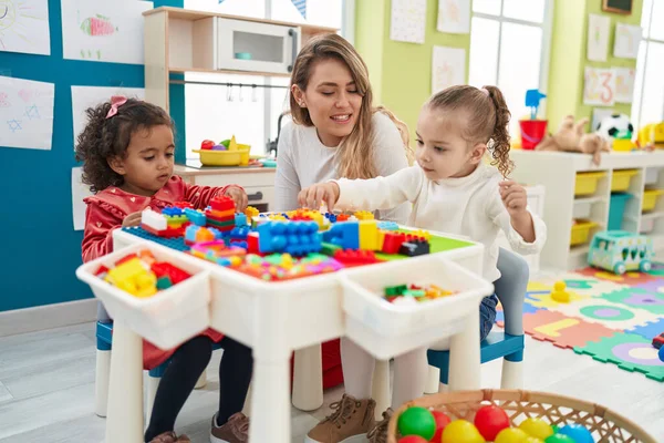 Teacher with girls playing with construction blocks sitting on table at kindergarten