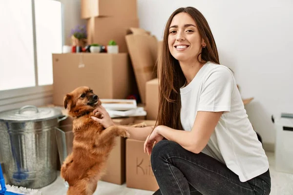 Young hispanic woman smiling confident playing with dog at new home