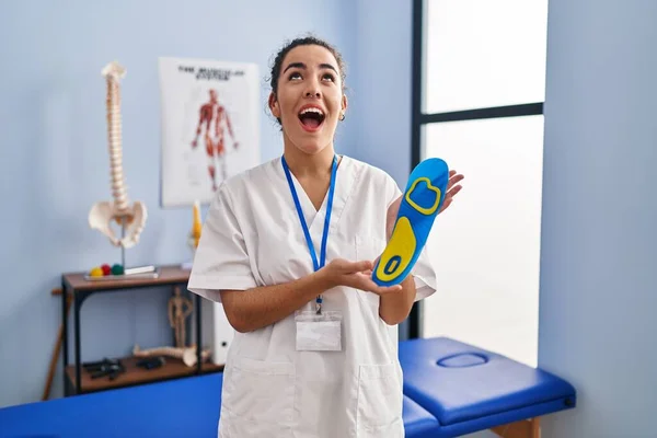 Young Hispanic Woman Holding Shoe Insole Physiotherapy Clinic Angry Mad — Stockfoto