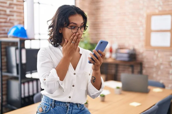 オフィスで働いている若いヒスパニック系の女性は 手で口をカバースマートフォンを使用して ショックを受け 間違いを恐れています 驚きの表情 — ストック写真