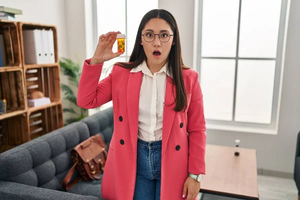 Young Latin Woman Working Therapist Holding Jar Pills Scared Amazed — Stockfoto