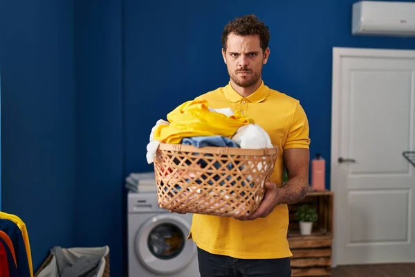 Young Hispanic Man Holding Laundry Basket Skeptic Nervous Frowning Upset — стоковое фото