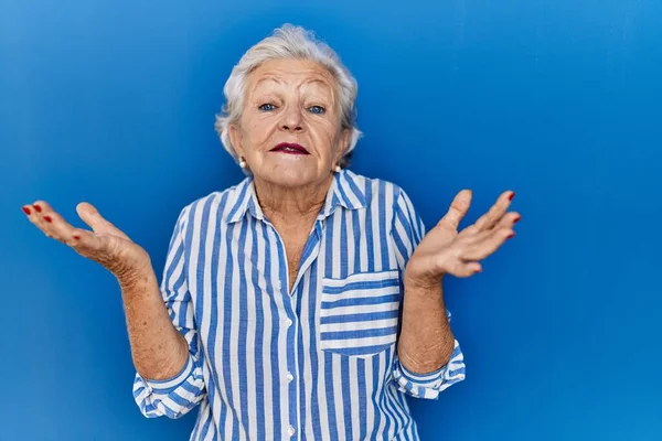 一个白发苍苍的老妇人站在蓝色的背景上 毫无头绪 满脸困惑 胳膊和双手高举 怀疑概念 — 图库照片