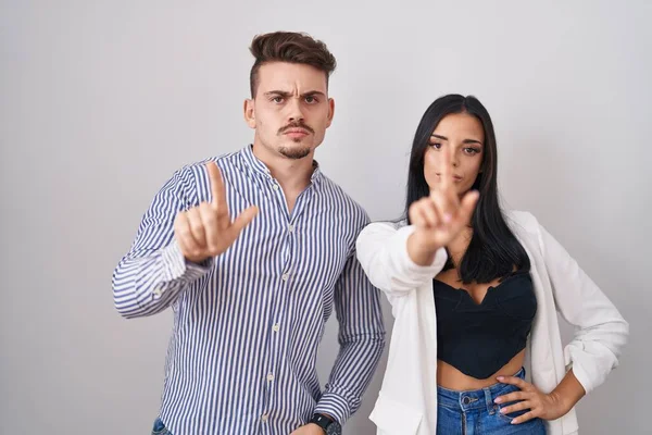 若いヒスパニック系のカップルが白い背景の上に立って指を指していると怒りの表情 ジェスチャーを示していません — ストック写真