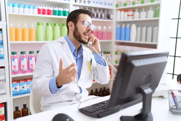 Young Hispanic Man Pharmacist Talking Telephone Using Computer Pharmacy — Stock Photo, Image