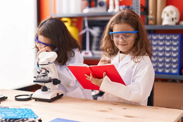 Two kids students using microscope writing on notebook at laboratory classroom