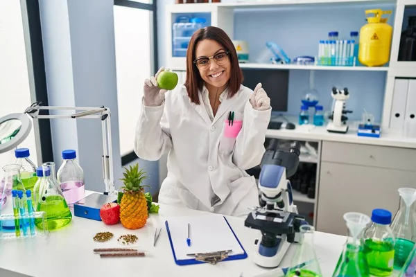 Young Hispanic Woman Working Scientist Laboratory Holding Fruit Screaming Proud — Stockfoto