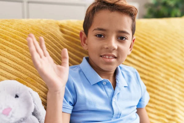 Adorable Hispanic Boy Saying Hello Hand Sitting Sofa Home — Fotografia de Stock