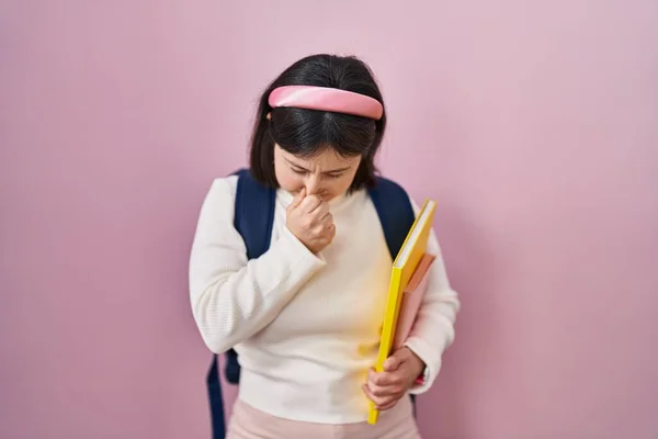 Woman with down syndrome wearing student backpack and holding books tired rubbing nose and eyes feeling fatigue and headache. stress and frustration concept.