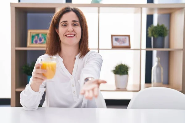 Brunette Woman Drinking Glass Orange Juice Smiling Cheerful Offering Palm — Fotografia de Stock