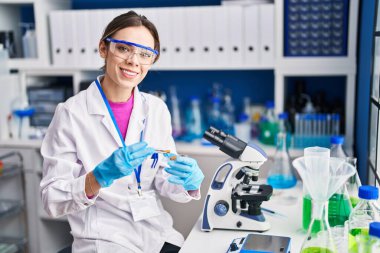 Young beautiful hispanic woman scientist smiling confident holding pill at laboratory