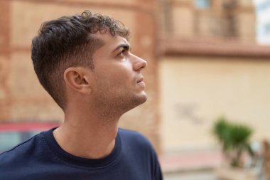 Latin kökenli genç adam ciddi bir ifadeyle sokağa bakıyor.