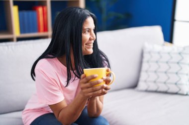 Orta yaşlı İspanyol kadın evdeki kanepede oturup kahve içiyor.