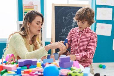 Teacher and toddler playing with geometry blocks sitting on table at kindergarten
