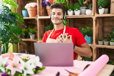 Young hispanic man working at florist shop doing video call smiling with hands on chest, eyes closed with grateful gesture on face. health concept. 