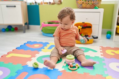 Adorable blond toddler playing with hoops toy sitting on floor at kindergarten