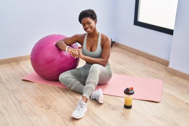 Spor merkezinde yoga minderinde oturan kronometre kullanan Afrikalı Amerikalı kadın.