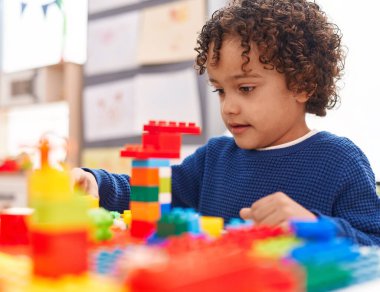 Anaokulundaki masada oturan, inşaat bloklarıyla oynayan sevimli İspanyol çocuk.