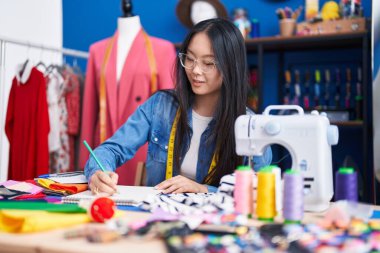 Genç Çinli kadın terzi. Kıyafet fabrikasında kendine güvenen çizimler yapıyor.