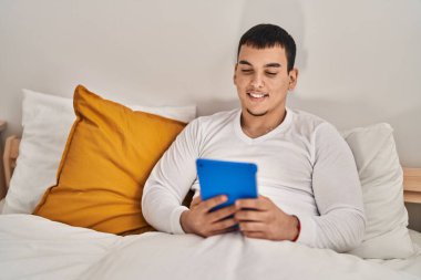 Yatak odasında dokunmatik ped kullanan genç bir adam.