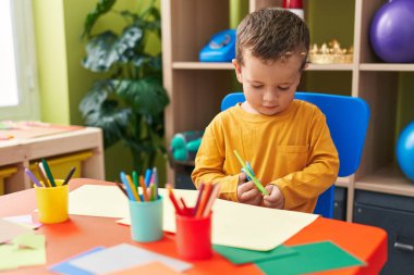 Anaokulunda masa başında kağıt kesen sevimli beyaz çocuk.