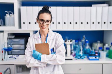 Young caucasian woman scientist smiling confident holding notebook at laboratory