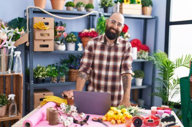 Young bald man florist smiling confident using laptop at flower shop