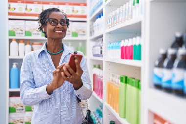 Orta yaşlı Afro-Amerikan kadın müşteri eczanede akıllı telefon kullanarak gülümsüyor.