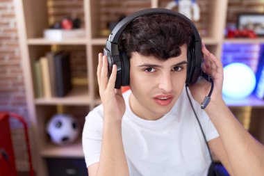Non binary man streamer sitting on table with relaxed expression at gaming room