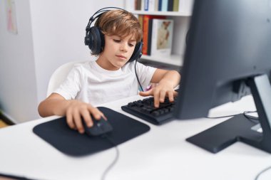 Sınıftaki masada bilgisayar kullanan sevimli beyaz çocuk.