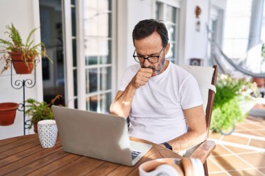Middle age man using computer laptop at home feeling unwell and coughing as symptom for cold or bronchitis. health care concept. 