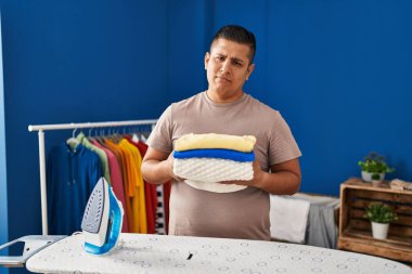 Hispanic young man holding folded laundry after ironing depressed and worry for distress, crying angry and afraid. sad expression. 