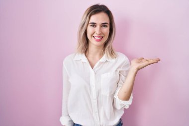 Pembe arka planda duran genç ve güzel bir kadın neşeli bir şekilde sunum yapıyor ve avuç içi kameraya bakıyor.. 