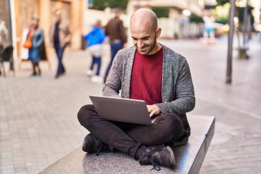 Genç adam dizüstü bilgisayar kullanıyor. Sokakta bankta oturuyor.