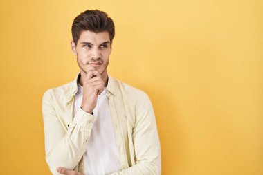 Sarı arka planda dikilen genç İspanyol bir adam bir soru hakkında endişeli ve gergin bir şekilde düşünüyor. 